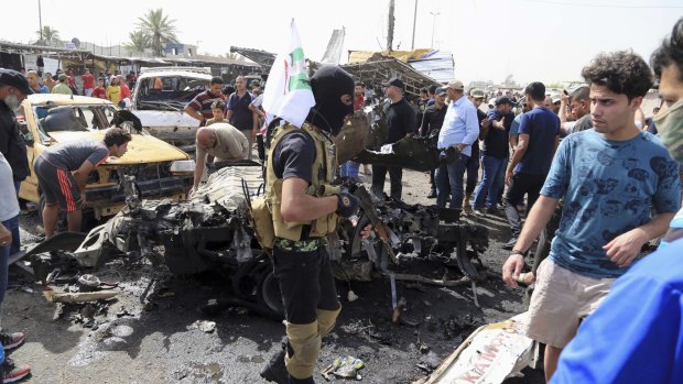 A masked member of an Iraqi Shiite fighters militant group called Kataib Peace Brigades, a Shiite militia group loyal to Shiite cleric Muqtada al-Sadr, centre, on the street with a flag after a suicide car bombing hit a crowded outdoor market in Sadr City on Tuesday. 