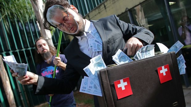 A demonstrator from the Avaaz organization wears a mask photograph of Eduardo Cunha, while holding a  briefcase stuffed with fake money outside Congress in Brasilia.