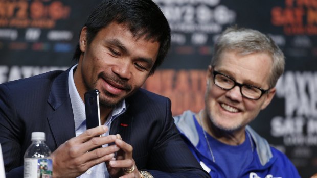 Pacquiao shows his phone to trainer Freddie Roach during the press conference.