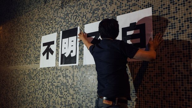 A Ming Pao staff member puts a sign up on a wall outside of Ming Pao headquarters in Hong Kong. 