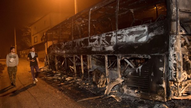 Residents walk past a burnt bus as a wildfire moves forward in Chandebrito in the north-western Spanish region of Galicia.