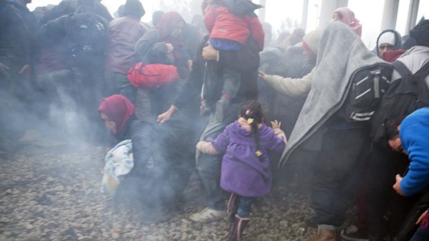 People run away after Macedonian police fired tear gas at a group of people who tried to push their way into Macedonia, breaking down a border gate near the northern Greek village of Idomeni on Monday.
