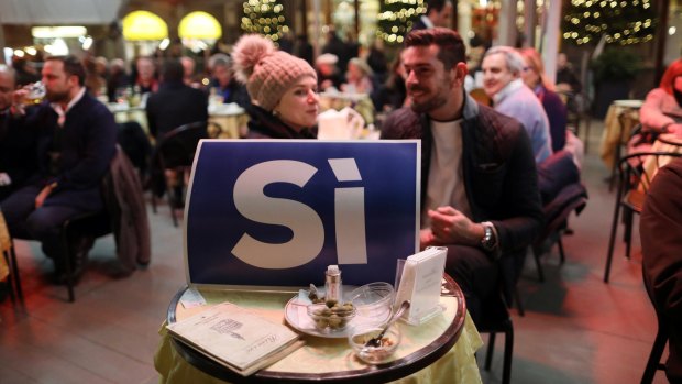 'Yes' campaign supporters eat dinner behind a poster in Florence.
