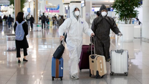 Travelers wearing protective masks and suits walk through Incheon International Airport in South Korea.