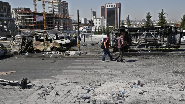 People walk past burnt and destroyed police and civilian vehicles near the presidential palace in Ankara, Turkey, on Sunday.