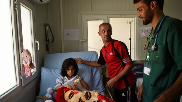 Mohamad Hazim, centre, and nurse Alaa Sulaiman, right, talk with Mohamad's daughter Taiba, 7, who suffered bone-deep shrapnel wounds and a broken leg. Five members of their family are still missing.