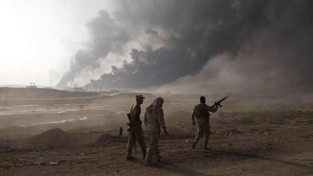 Iraqi soldiers man a checkpoint as oil wells burn on the outskirts of Qayara, near Mosul.  