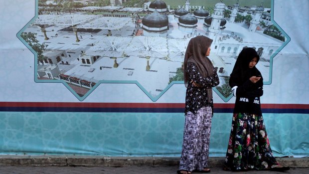 Acehnese girls stand near a banner showing an image of the Baiturrahman Grand Mosque in Banda Aceh on Friday. 