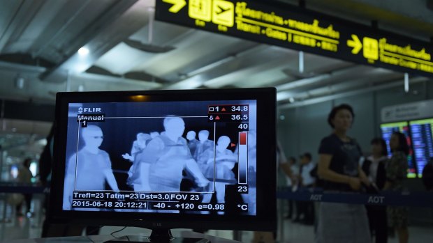 An airport employee monitors a screen as travellers walk past a thermoscan checking their body temperature on arrival at Bangkok's Suvarnabhumi Airport on Friday.