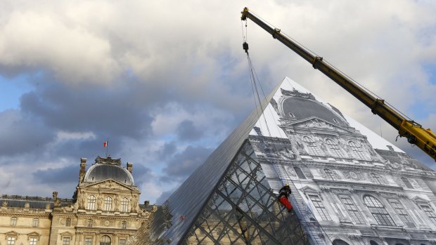 A technician pastes a giant picture on the Louvre Pyramid as part of JR's eye-tricking installation on Monday
