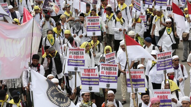 Marchers hold signs demanding that Ahok be jailed and that the Koran be defended.