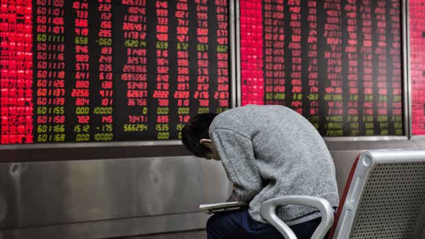 A man reads in front of an electronic board displaying share prices at a securities brokerage in Beijing.