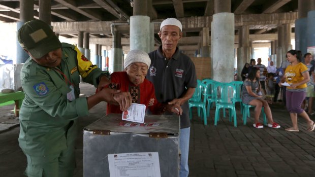 Electoral workers help an elderly woman cast her ballot at a makeshift polling station under a bridge.