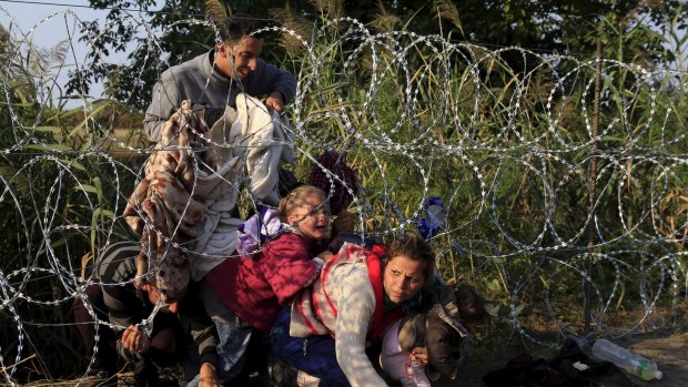 Syrian migrants wriggle under barbed wire to get into Hungary on Thursday. 
