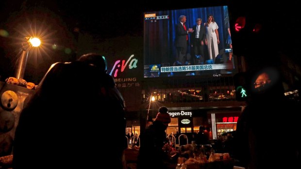 A woman walks past street vendors selling foods near a huge TV screen broadcasting US President-elect Donald Trump's victory speech in Beijing.