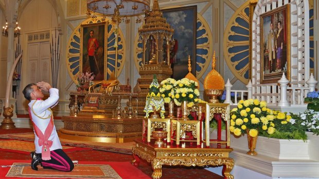 His Majesty King Maha Vajiralongkorn Bodindradebayavarangkun, or Rama X, kneels under a portrait of his late father at the Grand Palace in Bangkok, on Thursday.