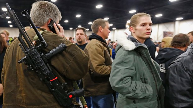 A man talks on a mobile phone while carrying a semi-automatic assault rifle he is trying to sell at the Rocky Mountain Gun Show in Sandy, Utah.