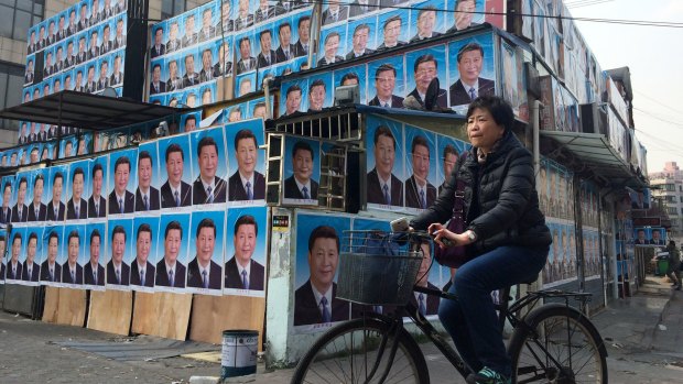 A woman cycles past a building covered in portraits of Chinese President Xi Jinping in Shanghai.