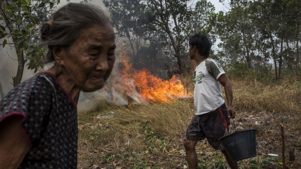 A man carries a bucket of water as he tries to extinguish a fire on burned peatland near his house in Ogan Ilir district, South Sumatra.