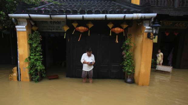Nguyen Huu Ngai looks at his phone in front of his flooded house in Hoi An ancient town.