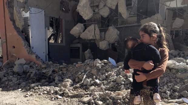 A young girl holds a child in front of a ruined house in Cizre, Turkey, on Wednesday. Turkish authorities on Wednesday scaled down a 24-hour curfew imposed on the mainly Kurdish town, nearly three weeks after declaring the successful conclusion of military operations there. 