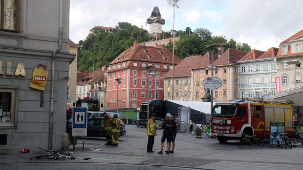 Firemen and police stand next to a damaged bicycle at the site where a man drove his van into a crowd at the main square in Graz, southern Austria, Saturday, June 20, 2015. According to officials three people were killed in the incident and 34 injured. 