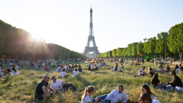 People sit and enjoy the sun in the Champs de Mars next to the Eiffel Tower in Paris.