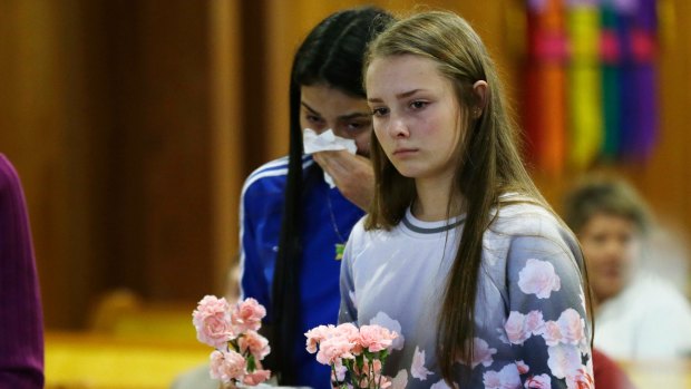 Rachel Marsh, 15, right, and Selena Orozco, 15, left, carry flowers as they attend a prayer service on Saturday for the victims of Friday's fatal shooting at a Macy's department store at the Cascade Mall in Burlington.