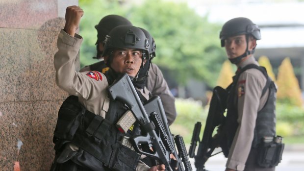 A police officer gives a hand signal to a squad mate as they search a building near the site of an explosion in Jakarta.