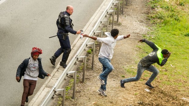 A police officer sprays tear gas as migrants try to access the Channel Tunnel on the A16 highway in Calais, northern France, on Wednesday.