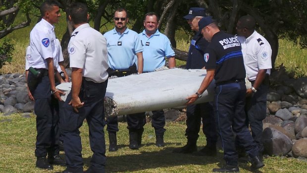 French gendarmes and police carry the piece of wing that was found on the beach on Reunion.