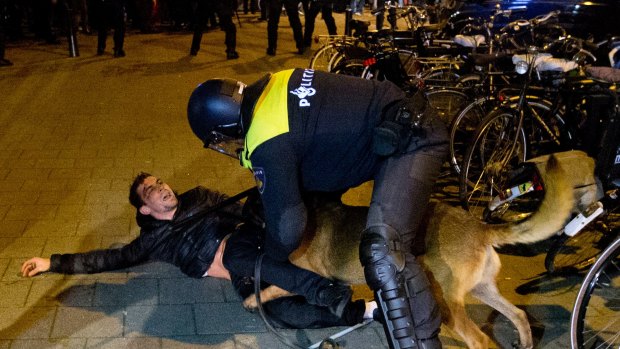 A Dutch riot policeman tries to get his dog to let go of a man after riots broke out at the Turkish consulate in Rotterdam.