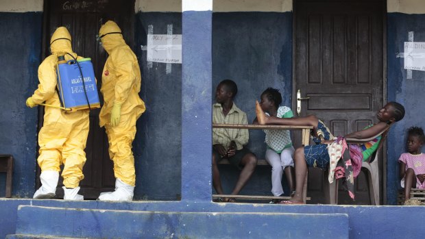 Residents of the village of Freeman Reserve, north of the Liberian capital Monrovia, watch ambulance officers disinfect a room where people with Ebola had been staying.