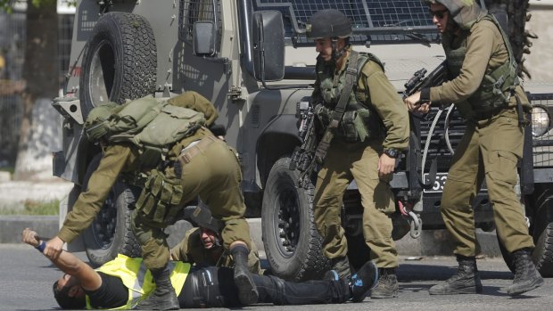 An Israeli soldier grabs the hand of a Palestinian holding a knife and wearing a "press" vest after he stabbed another Israeli soldier. A soldier later shot the man.