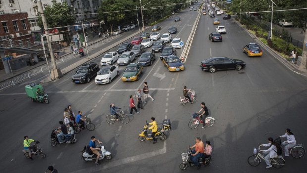 Cars, taxis, bikes, scooters and pedestrians converge at an intersection in Beijing.