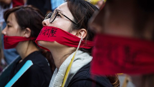 Demonstrators wear red bandannas across their mouths as they sit in protest during the rally.