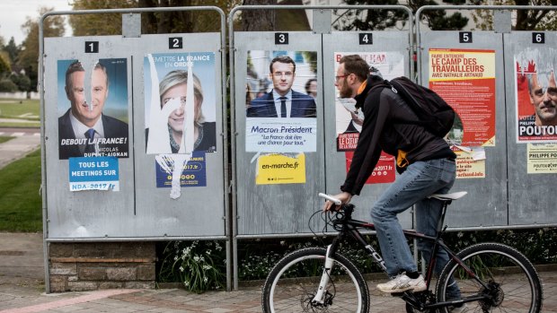 A cyclist passes by electoral campaign posters during the first round of the French presidential election in Le Touquet, France.