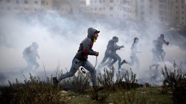 Palestinian protesters run for cover from tear gas fired by Israeli soldiers during clashes in Ramallah on Monday. 