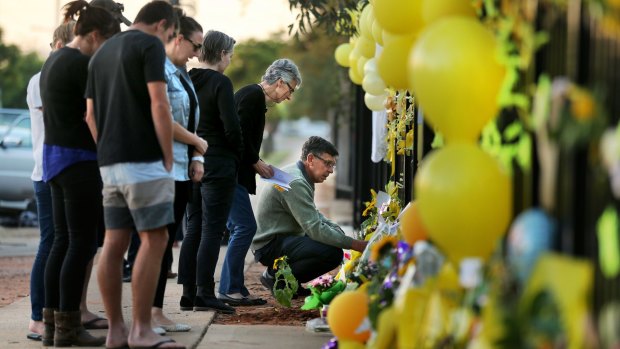 Merrilyn Scott (second from right) and Robert Scott (right), the parents of Stephanie Scott, examine the messages at the floral memorial on the gates of Leeton High School.