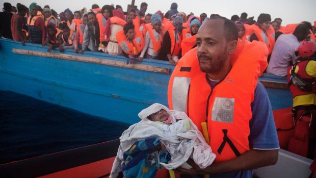 A man carries his five-day-old son onto an Italian vessel after been rescued from a crowded wooden boat fleeing Libya.