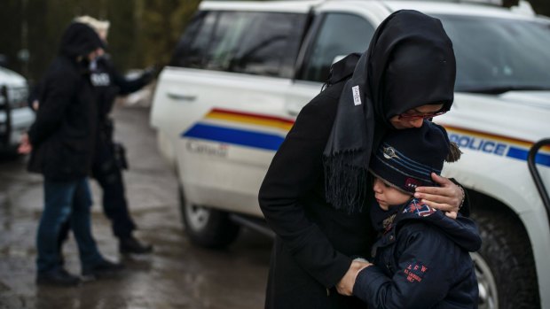 A woman comforts her son as his father is handcuffed by a Canadian police officer, having ignored the warning and crossed into Canada from Champlain, New York state.