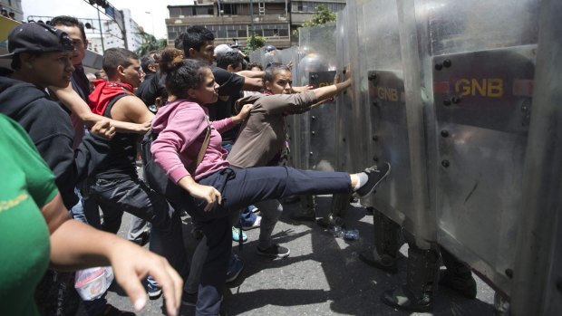 A woman kicks the shield of a National Guard soldier as others push them back them in Caracas.