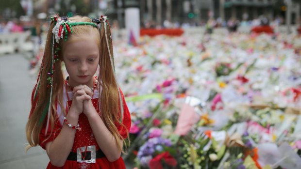 A young girl dressed in Christmas attire walks around the thousands of floral tributes on December 18, 2014 in Sydney.