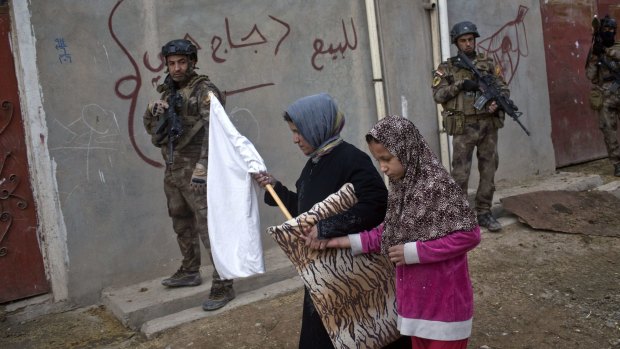 Civilians carry a white flag as they pass by Iraqi special forces on patrol in Gogjali, an eastern district of Mosul.