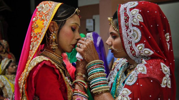 An Indian bride helps another with her attire during a mass wedding hosted by a diamond trader in Surat, India, last week.