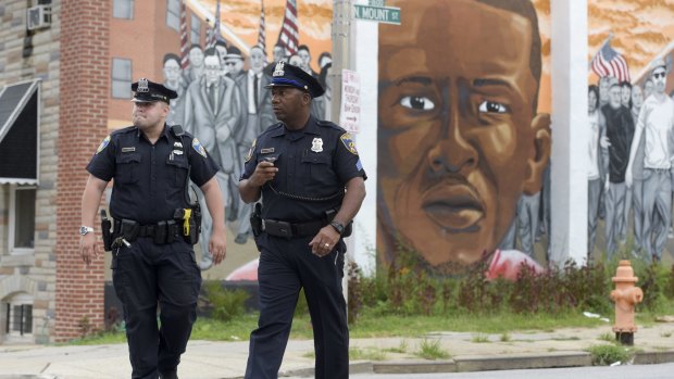 Baltimore police walk past a mural depicting Freddie Gray after prosecutors dropped remaining charges against the three officers still awaiting trial.