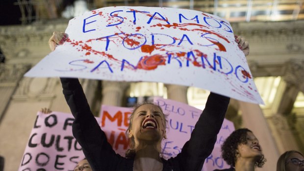 A woman shouts holding a banner that reads in Portuguese "We're all bleeding" to protest the rape of the 16-year-old girl. 