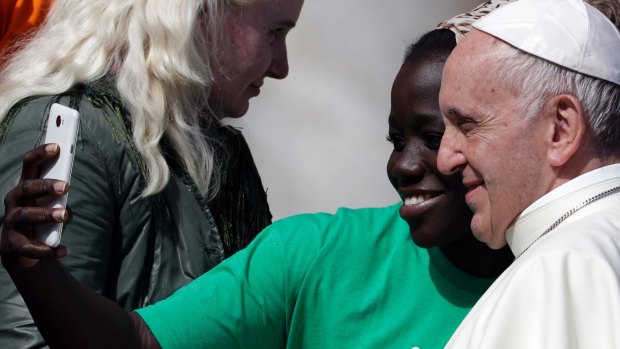 Pope Francis poses for a selfie with a migrant at the Vatican on Wednesday.