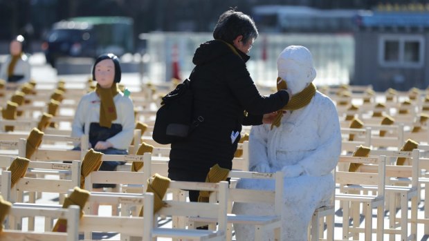 A woman puts a scarf on a statue of a comfort woman sitting in a installation of empty chairs symbolising sex slave victims in Seoul on Wednesday.