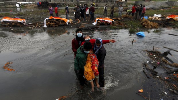 A Nepalese woman is carried after she fainted performing the last rites of her family members, who died in the earthquake.